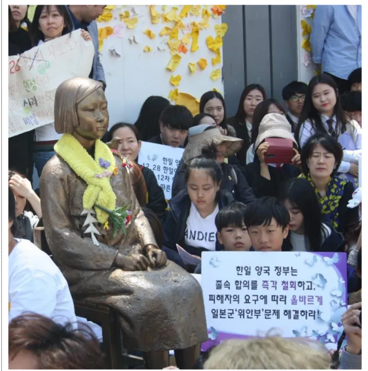Figura 3- Estátua da Paz (Peace Statue) erigida pelo Korean Council em 2011. Ao lado da estátua encontra-se  o  jovem  com  o  novo  cartaz  do  Korean  Council
