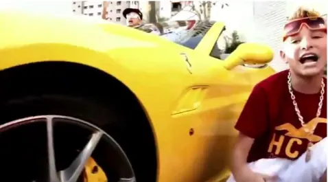 Figura 2: MC Gui canta ao lado de um automóvel em cena de videoclipe, sendo possível ver o logo da  marca Porsche 