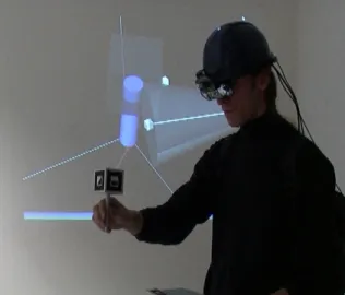 Figure 2.17: A user working in Construct3D wearing the AR kit while a live (monoscopic) video feed of his current construction is displayed (Kaufmann and Schmalstieg, 2002)