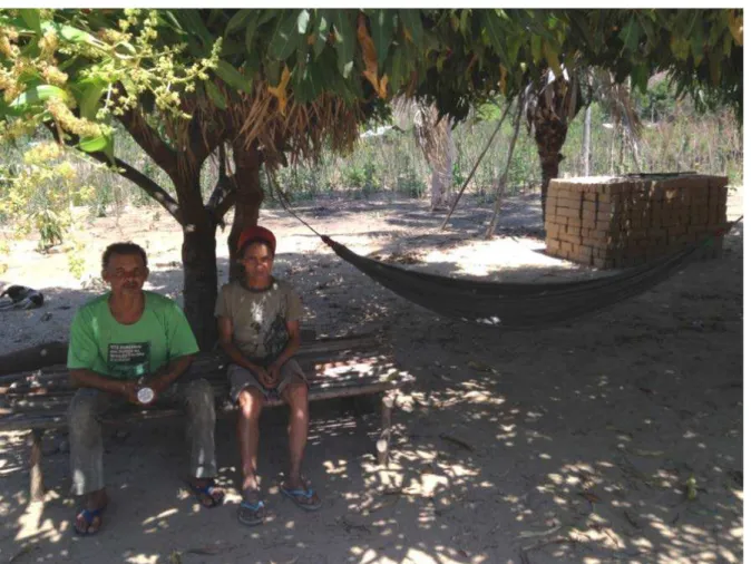 Foto 3 – Casal à sombra da mangueira, no jirau confeccionado com a madeira do buriti, com uma rede à sombra  do seu quintal e os adobes empilhados utilizados para a reforma da casa