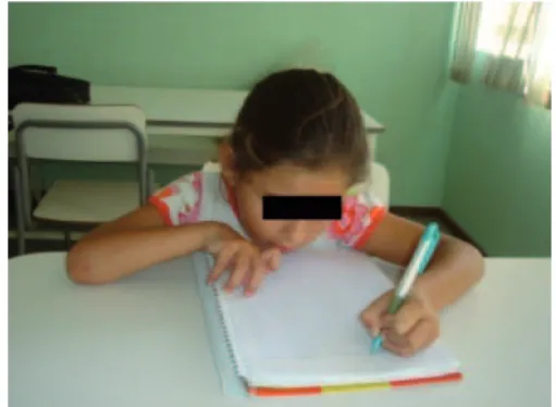 Figura 12 – Foto da aluna escrevendo  Figura  13  –  Foto  da  aluna  escrevendo  com a tala de punho