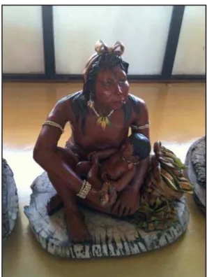 Foto 5 – Criança no colo da mãe que usa vários  braceletes e colar, manuseando espigas de  milho, base de sua alimentação.
