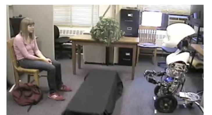 FIGURE 1 | A participant engaging in a 10-min conversation with a teleoperated humanoid robot, Nexi, here expressing the low-trust cue of hand touching.